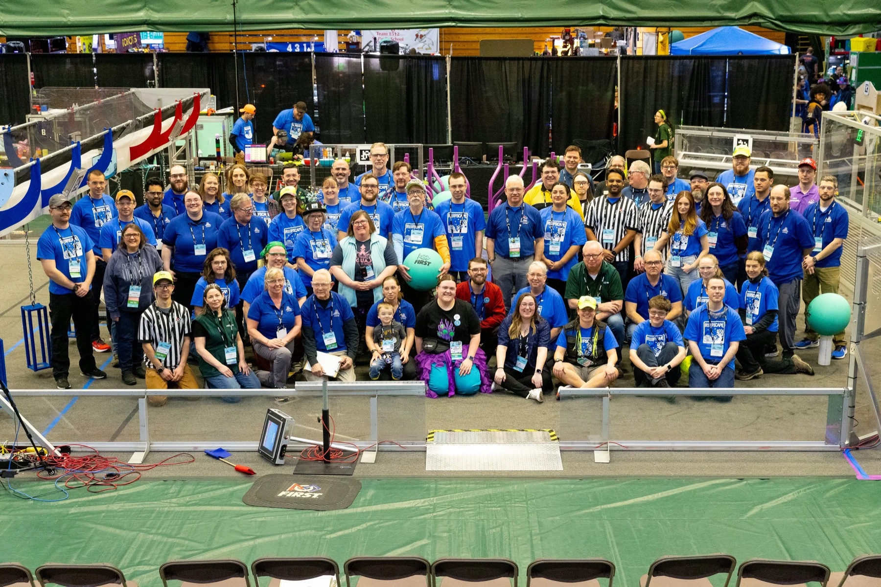 A large corporate volunteer group in matching shirts at a FIRST Robotics Competition event