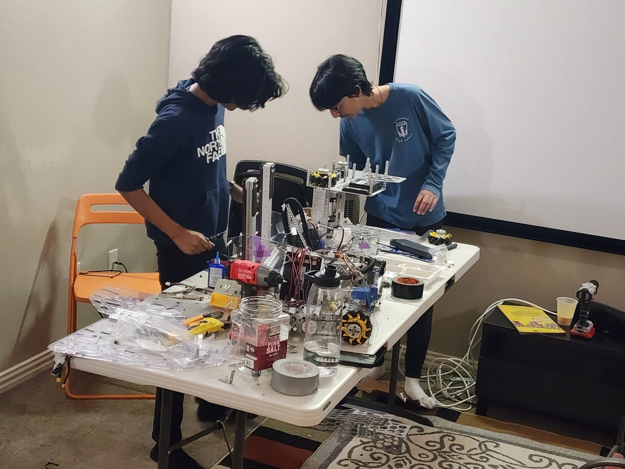 Two students working on the robot at a build table covered in tools and parts